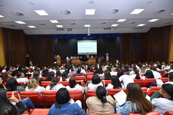 #PraCegoVer: Na imagem, funcionarios da saúde no Segundo Encontro em Defesa da Saúde da Mulher. Os funcionários estão em pé e a plateia sentada.